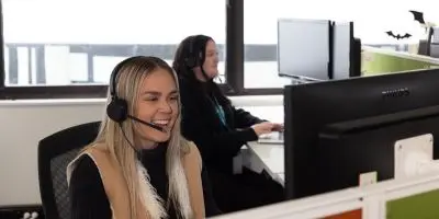 Two people at their desks, wearing headphones and engaged in phone conversations while also typing at their desktop computers