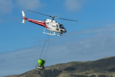 Helicopter flying over countryside with bucket underneath for 1080 drop