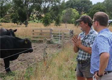 Two people talking in a field beside a cow enclosure