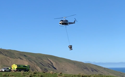 A helicopter with a hopper dispensing aerial 1080 baits over hilly terrain