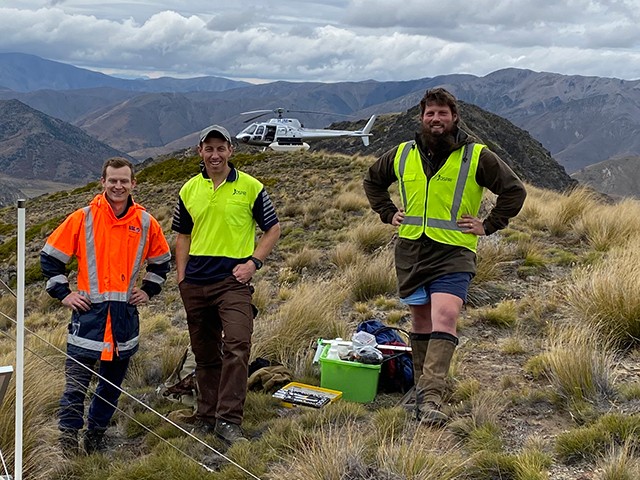 OSPRI staff atop a mountain, helicopter at the back.