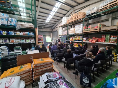 A group of farmers sitting in a warehouse, listening to OSPRI spokesperson.