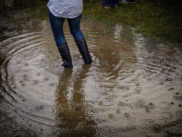 A person with gumboots standing in middle of a big puddle