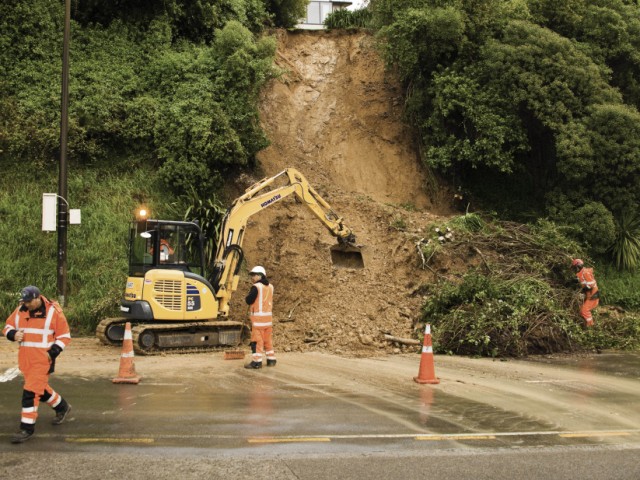 Roadworkers and a digger work on clearing a road after a slip