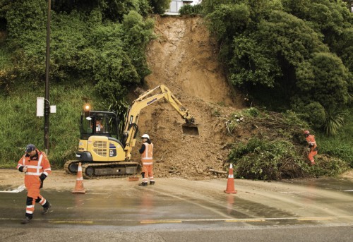 Roadworkers and a digger work on clearing a road after a slip