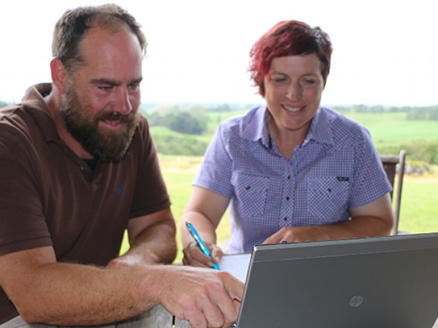 A couple looking at a laptop, taking notes; vast expanse of farm behind them