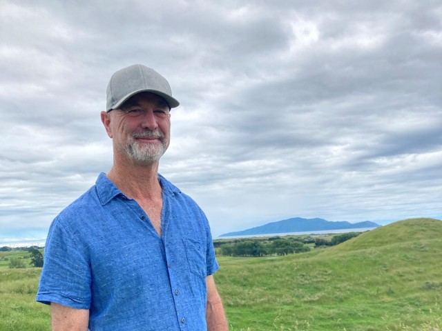 A man in a blue shirt and baseball cap standing in a green field.